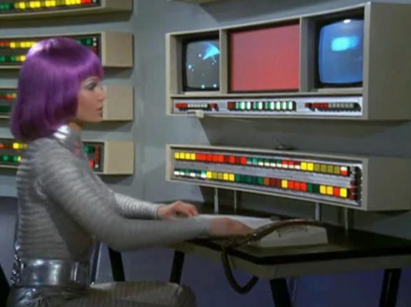 The Moonbase Beauties and Purple Wigs - The women stationed on the SHADO Moonbase are the ultimate icon of retro-chic sci-fi.
The Look – They wore tight, skin-tight metallic silver catsuits or ultra-short metallic miniskirts, complete with matching silver capes, heavy fake eyelashes, and bright, uniform bob-cut purple wigs.
The “Sci-Fi” Excuse – Producer Gerry Anderson claimed that under the harsh fluorescent lights of a lunar base, natural hair would look dull and create static electricity. Therefore, the purple wigs were supposedly “anti-static regulation gear.”
The Reality – The costume designer simply thought purple hair looked incredibly cool against the stark white walls of the moonbase set.
The Contrast - Moonbase Beauties vs. The Boys' Club
The way the show balanced sex appeal with this "advanced space team" is where the corporate logic gets really funny. On one side of the Moonbase, you have the female officers wearing heavy makeup, purple hair, and tight silver miniskirts. They are the ones tracking the alien radar and typing on the computers. But the moment a real fight starts, the show shifts to the three male pilots in their blue pajamas and matching silver motorcycle helmets.
It was a total reflection of 1970 society. The creators wanted the high-fashion, liberal visual hook of the "Moonbase Beauties" to get people to watch the screen, but when it came to the actual space battles, they reverted back to a traditional, serious military setup. The pilots didn't look sexy or futuristic – they looked like a highly trained bobsled team or racecar drivers.