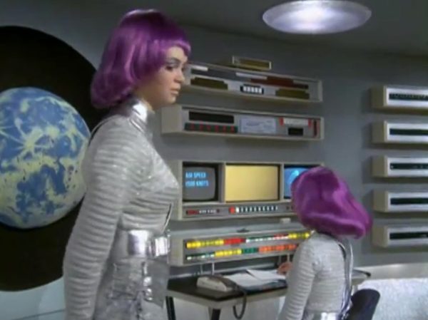 The Moonbase Beauties and Purple Wigs - The women stationed on the SHADO Moonbase are the ultimate icon of retro-chic sci-fi.
The Look - They wore tight, skin-tight metallic silver catsuits or ultra-short metallic miniskirts, complete with matching silver capes, heavy fake eyelashes, and bright, uniform bob-cut purple wigs.
The “Sci-Fi” Excuse - Producer Gerry Anderson claimed that under the harsh fluorescent lights of a lunar base, natural hair would look dull and create static electricity. Therefore, the purple wigs were supposedly “anti-static regulation gear”.
The Reality – The costume designer simply thought purple hair looked incredibly cool against the stark white walls of the moonbase set.
The Contrast - Moonbase Beauties vs. The Boys' Club
The way the show balanced sex appeal with this "advanced space team" is where the corporate logic gets really funny. On one side of the Moonbase, you have the female officers wearing heavy makeup, purple hair, and tight silver miniskirts. They are the ones tracking the alien radar and typing on the computers. But the moment a real fight starts, the show shifts to the three male pilots in their blue pajamas and matching silver motorcycle helmets.
It was a total reflection of 1970 society. The creators wanted the high-fashion, liberal visual hook of the "Moonbase Beauties" to get people to watch the screen, but when it came to the actual space battles, they reverted back to a traditional, serious military setup. The pilots didn't look sexy or futuristic – they looked like a highly trained bobsled team or racecar drivers.