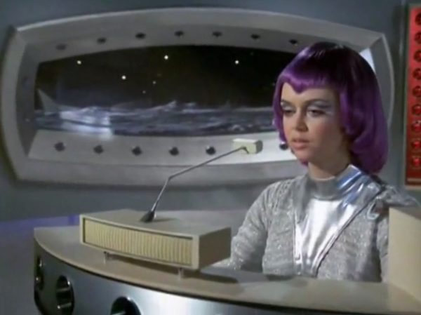 The Moonbase Beauties and Purple Wigs - The women stationed on the SHADO Moonbase are the ultimate icon of retro-chic sci-fi.
The Look - They wore tight, skin-tight metallic silver catsuits or ultra-short metallic miniskirts, complete with matching silver capes, heavy fake eyelashes, and bright, uniform bob-cut purple wigs.
The “Sci-Fi” Excuse - Producer Gerry Anderson claimed that under the harsh fluorescent lights of a lunar base, natural hair would look dull and create static electricity. Therefore, the purple wigs were supposedly “anti-static regulation gear”.
The Reality – The costume designer simply thought purple hair looked incredibly cool against the stark white walls of the moonbase set.
The Contrast - Moonbase Beauties vs. The Boys' Club
The way the show balanced sex appeal with this "advanced space team" is where the corporate logic gets really funny. On one side of the Moonbase, you have the female officers wearing heavy makeup, purple hair, and tight silver miniskirts. They are the ones tracking the alien radar and typing on the computers. But the moment a real fight starts, the show shifts to the three male pilots in their blue pajamas and matching silver motorcycle helmets.
It was a total reflection of 1970 society. The creators wanted the high-fashion, liberal visual hook of the "Moonbase Beauties" to get people to watch the screen, but when it came to the actual space battles, they reverted back to a traditional, serious military setup. The pilots didn't look sexy or futuristic – they looked like a highly trained bobsled team or racecar drivers.