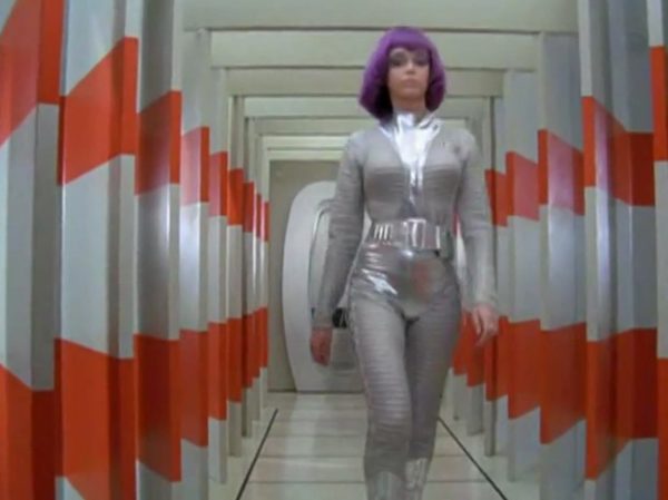 The Moonbase Beauties and Purple Wigs - The women stationed on the SHADO Moonbase are the ultimate icon of retro-chic sci-fi.
The Look - They wore tight, skin-tight metallic silver catsuits or ultra-short metallic miniskirts, complete with matching silver capes, heavy fake eyelashes, and bright, uniform bob-cut purple wigs.
The “Sci-Fi” Excuse - Producer Gerry Anderson claimed that under the harsh fluorescent lights of a lunar base, natural hair would look dull and create static electricity. Therefore, the purple wigs were supposedly “anti-static regulation gear”.
The Reality – The costume designer simply thought purple hair looked incredibly cool against the stark white walls of the moonbase set.
The Contrast - Moonbase Beauties vs. The Boys' Club
The way the show balanced sex appeal with this "advanced space team" is where the corporate logic gets really funny. On one side of the Moonbase, you have the female officers wearing heavy makeup, purple hair, and tight silver miniskirts. They are the ones tracking the alien radar and typing on the computers. But the moment a real fight starts, the show shifts to the three male pilots in their blue pajamas and matching silver motorcycle helmets.
It was a total reflection of 1970 society. The creators wanted the high-fashion, liberal visual hook of the "Moonbase Beauties" to get people to watch the screen, but when it came to the actual space battles, they reverted back to a traditional, serious military setup. The pilots didn't look sexy or futuristic – they looked like a highly trained bobsled team or racecar drivers.