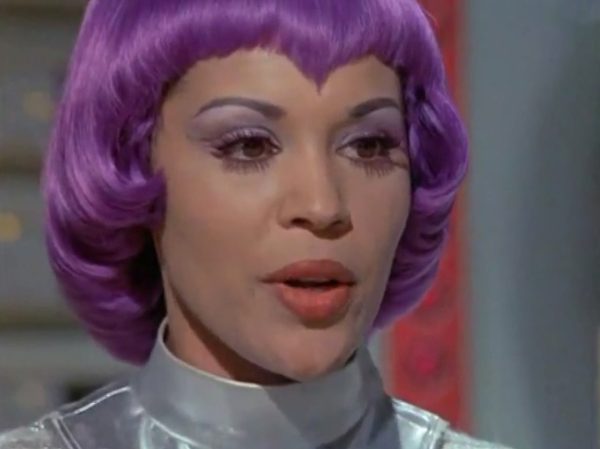 The Moonbase Beauties and Purple Wigs - The women stationed on the SHADO Moonbase are the ultimate icon of retro-chic sci-fi.
The Look - They wore tight, skin-tight metallic silver catsuits or ultra-short metallic miniskirts, complete with matching silver capes, heavy fake eyelashes, and bright, uniform bob-cut purple wigs.
The “Sci-Fi” Excuse - Producer Gerry Anderson claimed that under the harsh fluorescent lights of a lunar base, natural hair would look dull and create static electricity. Therefore, the purple wigs were supposedly “anti-static regulation gear”.
The Reality – The costume designer simply thought purple hair looked incredibly cool against the stark white walls of the moonbase set.
The Contrast - Moonbase Beauties vs. The Boys' Club
The way the show balanced sex appeal with this "advanced space team" is where the corporate logic gets really funny. On one side of the Moonbase, you have the female officers wearing heavy makeup, purple hair, and tight silver miniskirts. They are the ones tracking the alien radar and typing on the computers. But the moment a real fight starts, the show shifts to the three male pilots in their blue pajamas and matching silver motorcycle helmets.
It was a total reflection of 1970 society. The creators wanted the high-fashion, liberal visual hook of the "Moonbase Beauties" to get people to watch the screen, but when it came to the actual space battles, they reverted back to a traditional, serious military setup. The pilots didn't look sexy or futuristic – they looked like a highly trained bobsled team or racecar drivers.