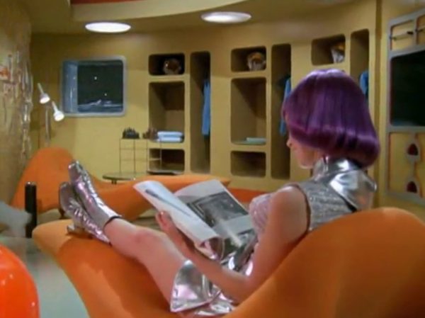 The Moonbase Beauties and Purple Wigs - The women stationed on the SHADO Moonbase are the ultimate icon of retro-chic sci-fi.
The Look - They wore tight, skin-tight metallic silver catsuits or ultra-short metallic miniskirts, complete with matching silver capes, heavy fake eyelashes, and bright, uniform bob-cut purple wigs.
The “Sci-Fi” Excuse - Producer Gerry Anderson claimed that under the harsh fluorescent lights of a lunar base, natural hair would look dull and create static electricity. Therefore, the purple wigs were supposedly “anti-static regulation gear”.
The Reality – The costume designer simply thought purple hair looked incredibly cool against the stark white walls of the moonbase set.
The Contrast - Moonbase Beauties vs. The Boys' Club
The way the show balanced sex appeal with this "advanced space team" is where the corporate logic gets really funny. On one side of the Moonbase, you have the female officers wearing heavy makeup, purple hair, and tight silver miniskirts. They are the ones tracking the alien radar and typing on the computers. But the moment a real fight starts, the show shifts to the three male pilots in their blue pajamas and matching silver motorcycle helmets.
It was a total reflection of 1970 society. The creators wanted the high-fashion, liberal visual hook of the "Moonbase Beauties" to get people to watch the screen, but when it came to the actual space battles, they reverted back to a traditional, serious military setup. The pilots didn't look sexy or futuristic – they looked like a highly trained bobsled team or racecar drivers.